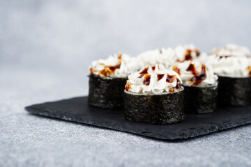 Savory sushi rolls topped with creamy sauce on a slate platter