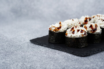 Sushi rolls with cream and sauce on a sleek slate platter