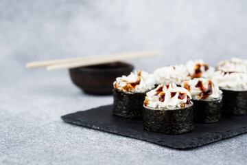 Sushi rolls with creamy topping served on dark plate at modern dining setting