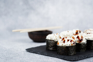 Unique sushi rolls with cream topping on a slate plate with chopsticks nearby