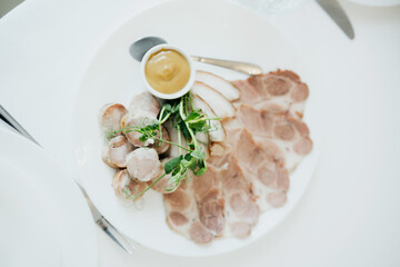 Cured meat platter with mustard on a white plate at a dining table