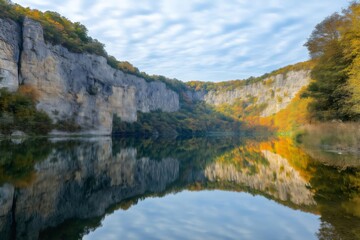 Autumn colored trees and rugged rocks reflecting beautifully on the calm waters of a serene mountain lake create a picturesque landscape