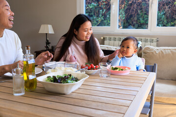 Toddler making a funny face looking at camera while parents laugh at the table