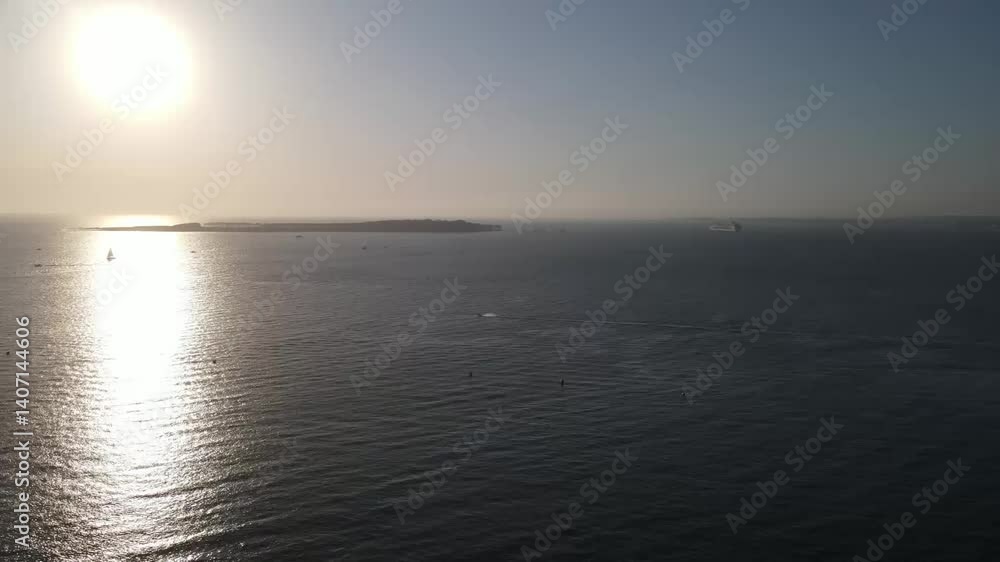 Aufkleber unlight reflects on a tranquil ocean, creating a shimmering path towards a distant island, with sail