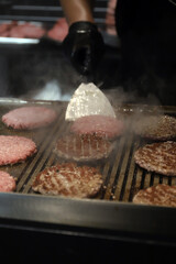 chef cocinando hamburguesas de carne a la parrilla y dándoles la vuelta con una paleta de cocina