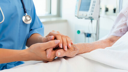 Mitfühlende Pflegerin hält die Hand eines älteren Patienten am Krankenbett
