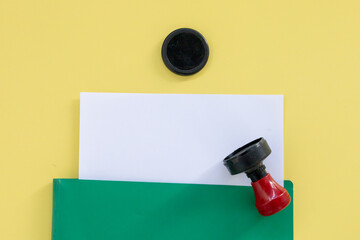 Document Review: Green Folder, Blank Page, and Unmarked Stamp, Set on Yellow Background