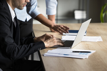 Close-up of hands. Two formal office coworkers discuss online project using laptop, work together. Mature experienced mid-aged lady boss coaches young colleague partner. Cooperation brainstorm concept
