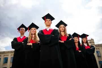 Confident graduates standing proudly in academic attire during a sunny day on campus, celebrating...