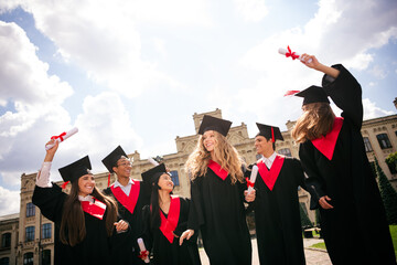 Joyful graduates celebrate together outdoors on a sunny day.
