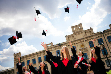 Joyful graduates celebrate outdoors, throwing mortarboards skyward, marking the conclusion of their...