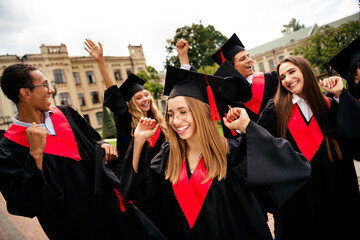 Joyful students celebrating graduation in traditional academic attire on a university campus during...