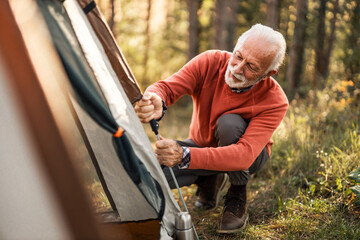 Older Man Sets Up Tent in Forest During Camping Adventure