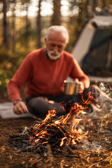 Elderly Camper Sitting by Fire in Forest Setting