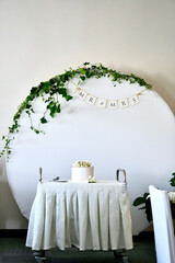 Weeding cake with letters V and M on the serving table against the background of a photo area for newlyweds.