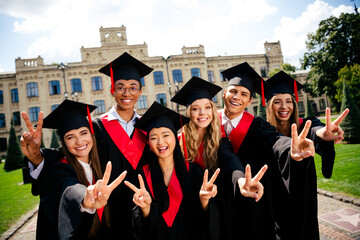 Portrait of group students mortarboard smile show v-sign gown graduation university building...