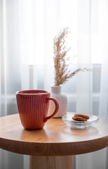 Cozy coffee setup with cookies and dried flowers on wooden table in living room.