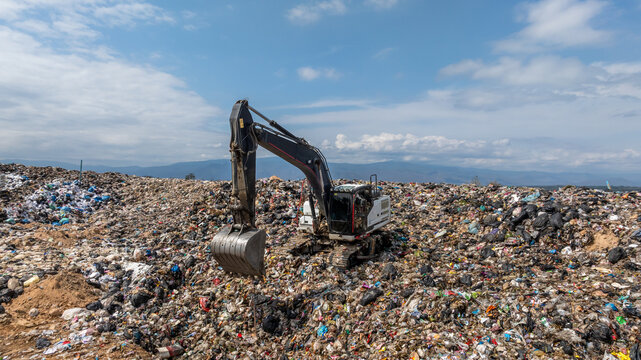 Bulldozer working on massive lanfill waste site with mountain background, Heavy machinery manage plastic waste at larg garbage dump, Excavtor at landfill global waste crisis concept.