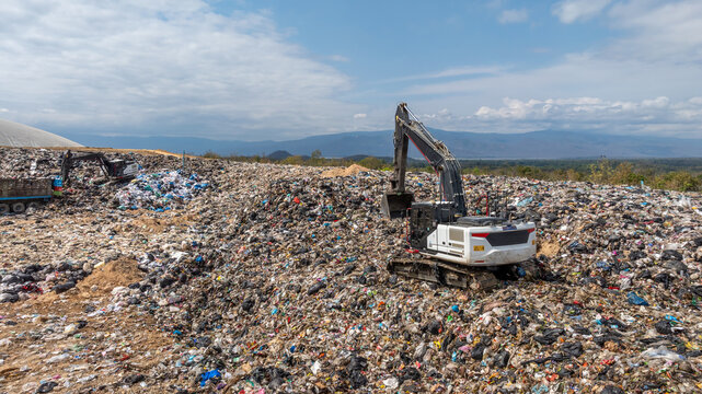 Bulldozer working on massive lanfill waste site with mountain background, Heavy machinery manage plastic waste at larg garbage dump, Excavtor at landfill global waste crisis concept.