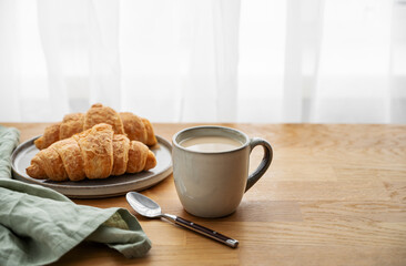 Cup of coffee with milk and fresh croissants  on a wooden table with napkin