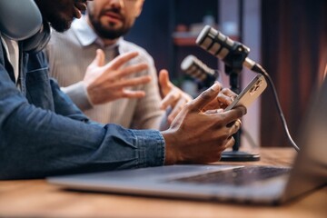 Focused close up view, holding smartphone. Two radio presenters recording an audio broadcast in a studio