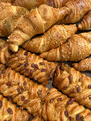 A close-up view of an assortment of freshly baked croissants featuring different toppings like sesame seeds and nuts, showcasing their flaky textures and appetizing appearance.