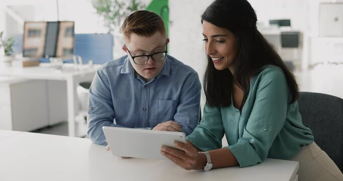 Two diverse colleagues working in inclusive company with accessible environment, using tablet together, testing online product, application, discussing algorithm, smiling, laughing
