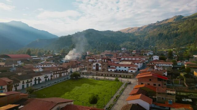 A panoramic view of Chacas' central square in the Peruvian highlands. As the drone pulls back, traditional houses come into view, framed by majestic mountains under a clear sky.