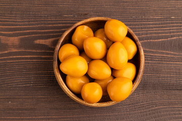 Pile of smoked quail eggs in bowl on a brown wooden background. top view