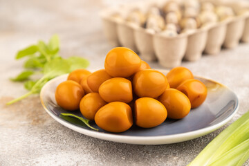 Pile of smoked quail eggs on plate on a brown concrete background. side view, close up, selective focus.