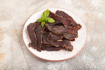 Armenian Basturma dried meat on plate with pepper and herbs on brown concrete. Side view