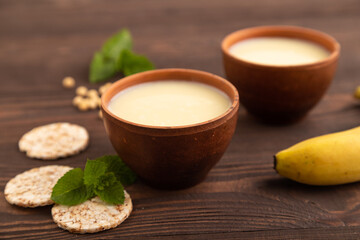 Organic non dairy banana and soy milk in clay cup on brown wooden, side view, selective focus.