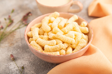 Corn flakes sticks with caramel in ceramic bowl on gray concrete, side view, close up.