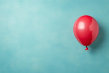 Fototapeta premium Vibrant red balloon with a glossy finish positioned on the left, creating a cheerful atmosphere against a soft pastel blue background with room for text