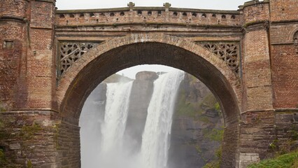 A large stone railway bridge spanning a river and a waterfall, providing access to a mountainous region.