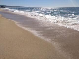 A serene beach at midday with gentle waves lapping the shore and clear blue skies inviting relaxation