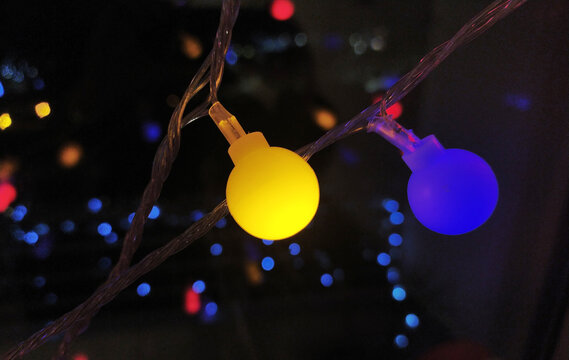 Close-up of vibrant yellow and blue LED lights on a string, creating a festive and modern bokeh effect against a dark background.