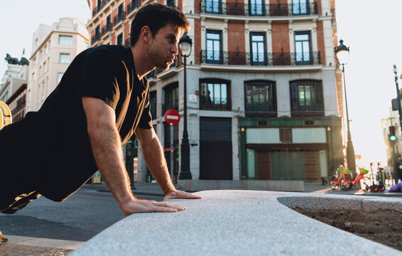 Sporty young man working out on urban bench, performing push-ups during golden hour in quiet city, focused and disciplined in his early fitness routine