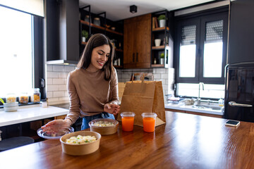 Happy woman unpacking a delicious takeaway food order in a stylish modern kitchen, enjoying the...