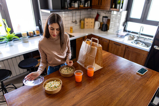 Young woman unpacking a delicious takeaway food order in a stylish, modern kitchen, preparing for a satisfying meal at home