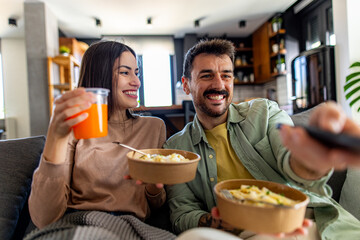 Happy couple eating pasta from takeaway boxes and watching television, enjoying their free time...
