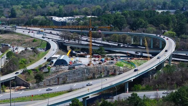 Interstate traffic and elevated highway during sunny day in Atlanta Suburb. Aerial wide shot. Yellow crane on construction site. Spring day in USA.