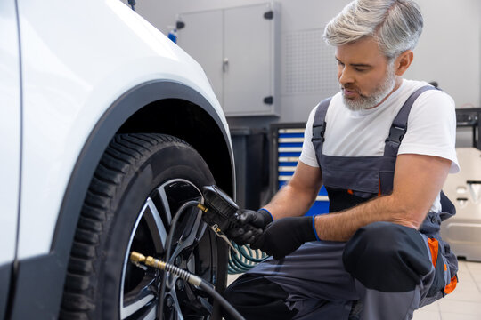 Gray haired mechanic checking tires air with pressure gauge