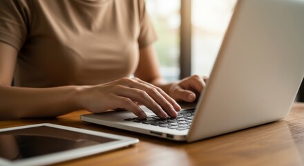 Focused professional typing on laptop with tablet on desk in modern workspace