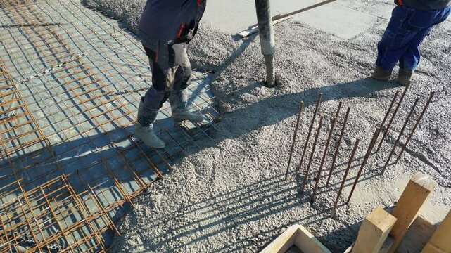 Construction workers with concrete boom pump crane at construction site pouring concrete into a formwork with reinforcement for building a new house, high angle view