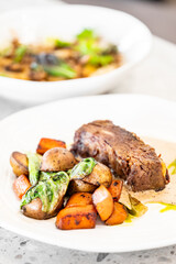 A hearty plate featuring tender beef alongside roasted potatoes, carrots, and sautéed greens, drizzled with a creamy sauce. The vibrant dish highlights a delicious dining experience.
