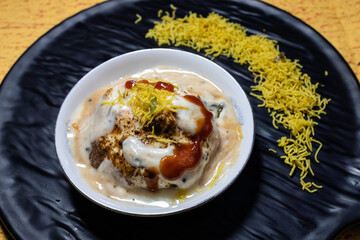 A flavorful Indian chaat dahi vada or dahi bhalla served with yogurt, tamarind chutney, and crispy toppings served on elegant black platter. Ideal for showcasing traditional cuisine and tasty snacks.