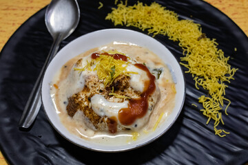 A flavorful Indian chaat dahi vada or dahi bhalla served with yogurt, tamarind chutney, and crispy toppings served on elegant black platter. Ideal for showcasing traditional cuisine and tasty snacks.