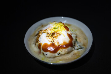 A flavorful Indian chaat dahi vada or dahi bhalla served with yogurt, tamarind chutney, and crispy toppings served on elegant black platter. Ideal for showcasing traditional cuisine and tasty snacks.