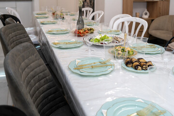 A beautifully arranged dining table awaits guests, adorned with delicate plates and glasses. A variety of dishes showcase vibrant food, creating a warm atmosphere for celebration.